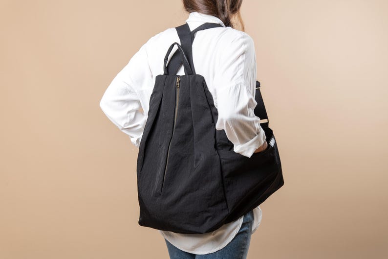 Puede incluir: Una persona con una camisa blanca y una mochila negra. La mochila tiene una cremallera y una solapa.