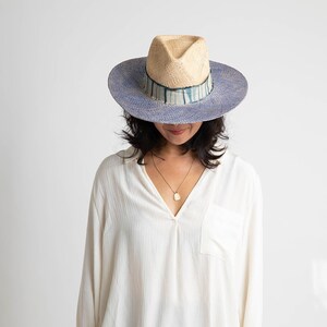 May include: A woman wearing a white shirt with a blue and white striped hat. The hat has a wide brim and a light brown crown.