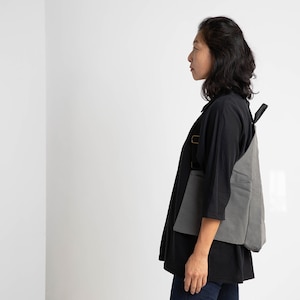 Puede incluir: Una mujer con una camisa negra y pantalones vaqueros azules con una mochila de lona gris.