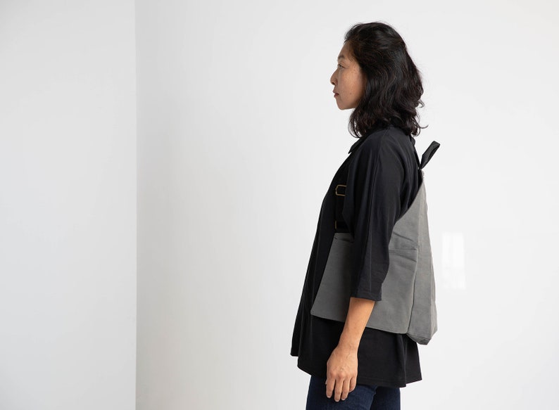 Puede incluir: Una mujer con una camisa negra y pantalones vaqueros azules con una mochila de lona gris.