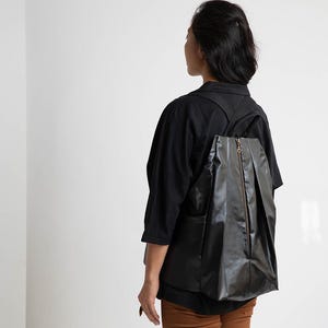 May include: A person wearing a black shirt and brown trousers with a black rucksack. The rucksack has a zipper and a pleated design.