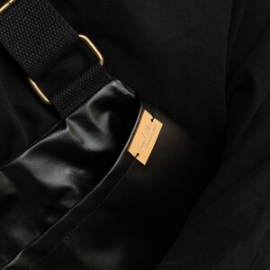 Puede incluir: Bolso bandolera negro con una correa negra y herrajes met&aacute;licos dorados. El bolso est&aacute; hecho de un material brillante y liso. Una peque&ntilde;a etiqueta rectangular de color marr&oacute;n claro est&aacute; adherida al bolso.