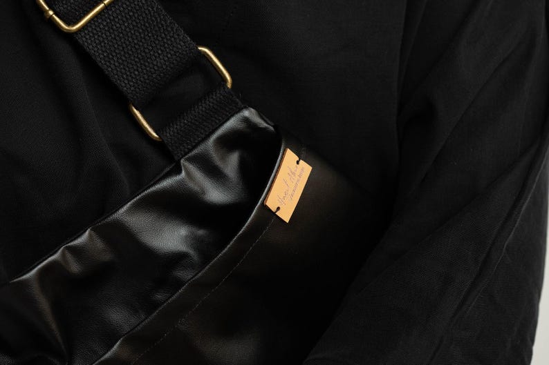 Puede incluir: Bolso bandolera negro con una correa negra y herrajes met&aacute;licos dorados. El bolso est&aacute; hecho de un material brillante y liso. Una peque&ntilde;a etiqueta rectangular de color marr&oacute;n claro est&aacute; adherida al bolso.