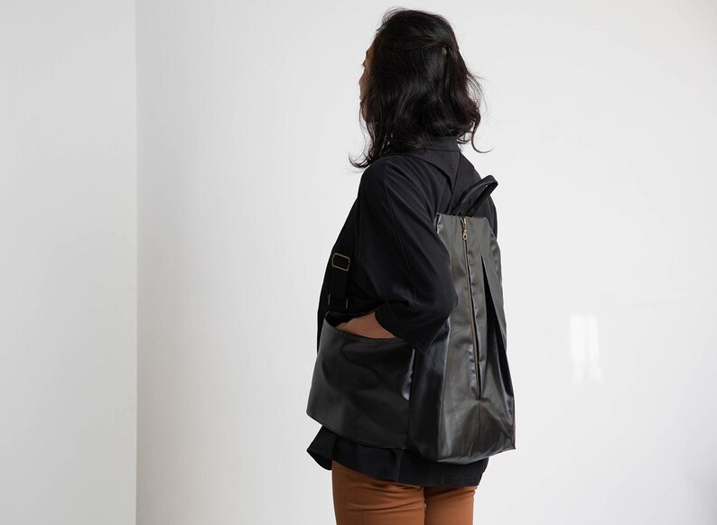 May include: A person wearing a black shirt and brown trousers with a black leather rucksack. The rucksack has a zip and a flap.