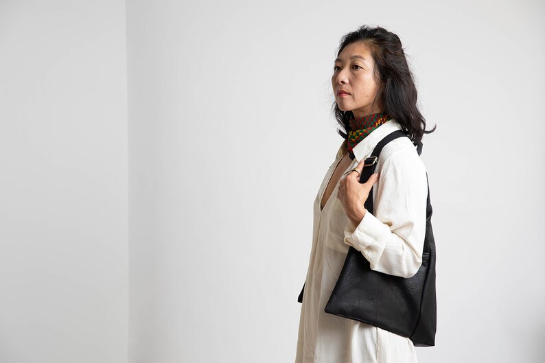 May include: A woman wearing a white shirt and a patterned scarf is holding a black leather tote bag.