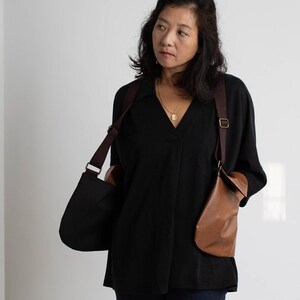 Puede incluir: Una blusa negra con cuello en V y dos bolsos de cuero para el hombro. Los bolsos son marrones y negros, con correas ajustables. La mujer lleva un collar de oro.