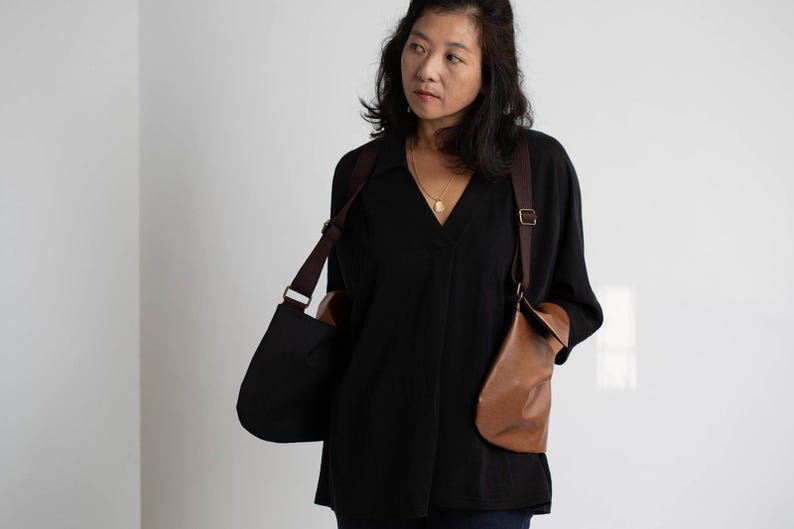 Puede incluir: Una blusa negra con cuello en V y dos bolsos de cuero para el hombro. Los bolsos son marrones y negros, con correas ajustables. La mujer lleva un collar de oro.