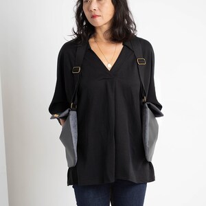 Puede incluir: Top negro con cuello en V y mangas largas, combinado con vaqueros azul oscuro. El conjunto incluye un bolso gris &uacute;nico con correas negras y herrajes met&aacute;licos dorados.