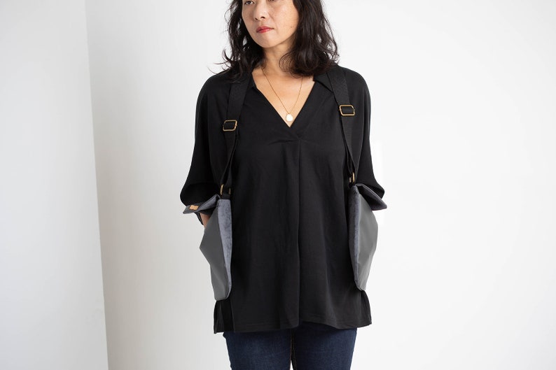 Puede incluir: Top negro con cuello en V y mangas largas, combinado con vaqueros azul oscuro. El conjunto incluye un bolso gris &uacute;nico con correas negras y herrajes met&aacute;licos dorados.