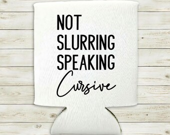 May include: White drinks can cooler featuring the words "NOT SLURRING SPEAKING Cursive" in black. The cooler has a cut-out at the bottom and is set against a light wood grain background.