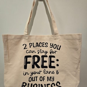 May include: A white canvas tote bag with black text that reads "2 PLACES YOU can stay for FREE: in your lane & OUT OF MY BUSINESS".