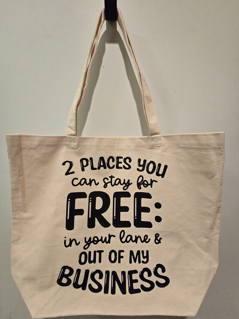 May include: A white canvas tote bag with black text that reads "2 PLACES YOU can stay for FREE: in your lane & OUT OF MY BUSINESS".