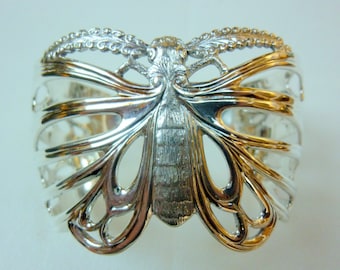 May include: Silver butterfly napkin ring with an intricate design. The ring is made of a delicate, openwork metal and features a detailed butterfly design.