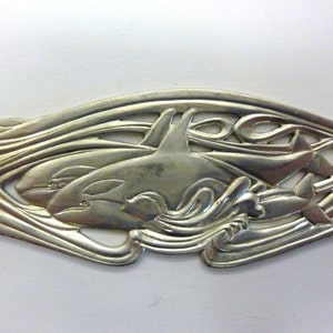 May include: Silver-toned metal ornament featuring two orcas swimming through stylized waves. The orcas are detailed with realistic features and the waves are intricate and flowing.