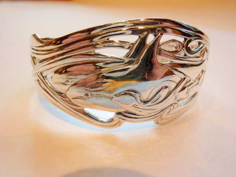 May include: Silver bracelet with a detailed design of two dolphins swimming in waves.