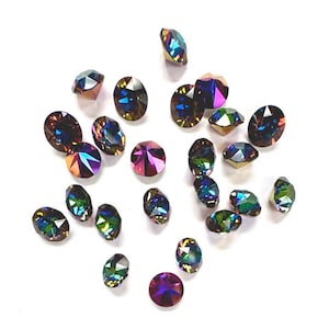May include: A collection of iridescent rhinestones in various shapes, including oval and faceted cuts. The gems display a range of colors, such as purple, green, and gold, against a white background. These decorative stones are suitable for crafts and embellishments.