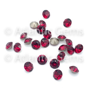 May include: A scattering of red crystal rhinestones on a white background. The rhinestones are round and have a faceted design.