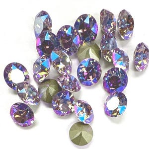 May include: A collection of iridescent purple rhinestones, some with a silver backing, scattered on a white surface.
