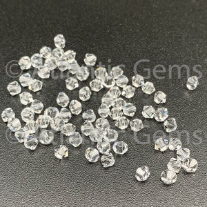 May include: A close-up of a pile of clear glass beads. The beads are small and have a faceted design. They are scattered on a black surface.