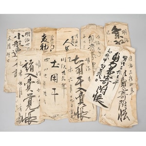 May include: A collection of ten rectangular, off-white paper documents featuring black ink calligraphy. Each piece of paper displays unique handwritten Japanese characters, dates, and vertical text arrangements, showing signs of age and texture.
