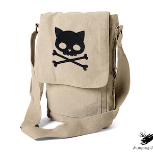 May include: A beige canvas messenger bag with a black cat skull and crossbones design.