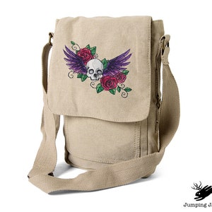 May include: A beige canvas messenger bag with an embroidered design of a skull with wings and roses.