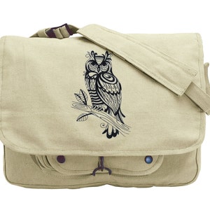 May include: A beige canvas messenger bag with a black and white owl design. The owl is perched on a branch and has intricate details.