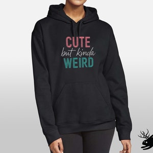 May include: Black hooded sweatshirt with the text "Cute but kinda weird" in pink and teal lettering.