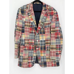 May include: A blazer featuring a patchwork design composed of various plaid and tartan patterns in shades of red, navy blue, yellow, green, and white. The garment includes a notched lapel, two front buttons, and four buttons on each sleeve cuff.