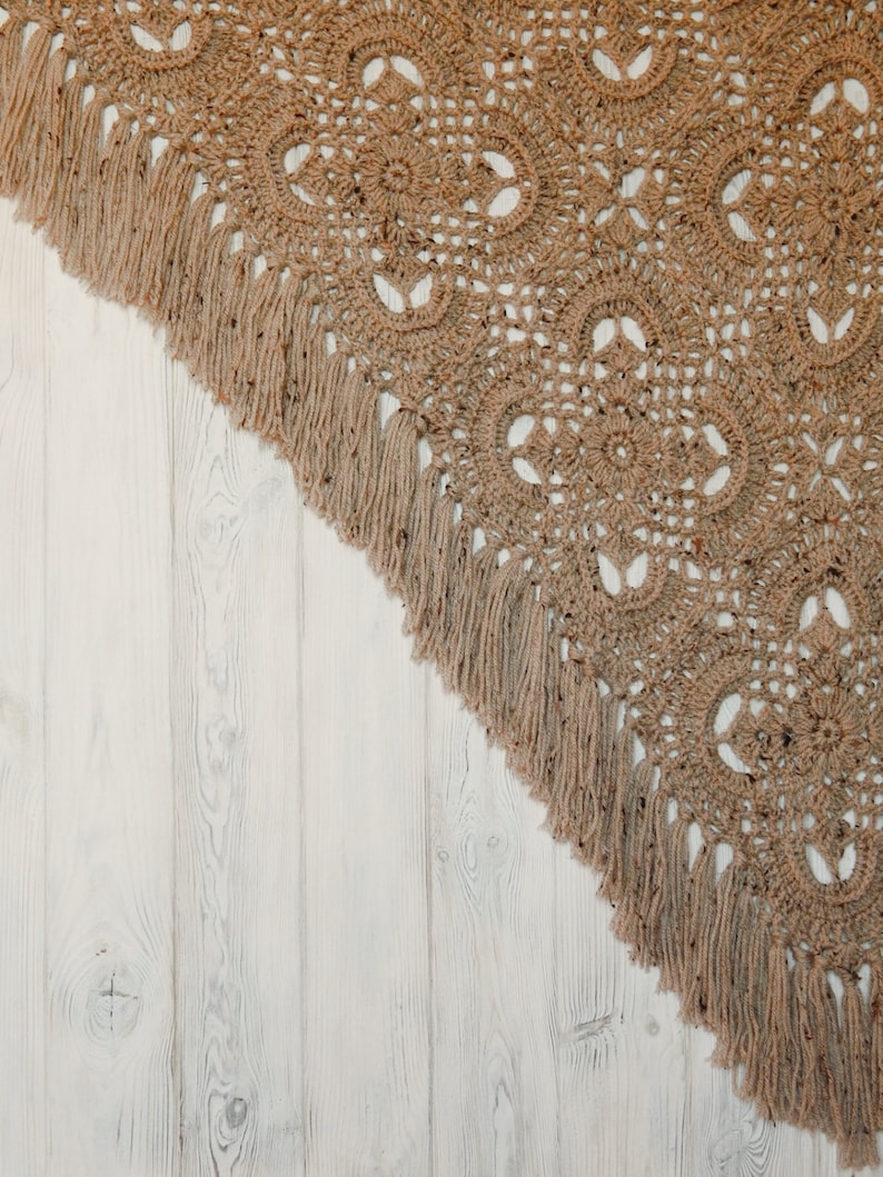 May include: A brown crocheted throw blanket with fringe on a white wood background.