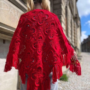 May include: A red crocheted shawl with fringe. The shawl has a delicate pattern and is made with a soft yarn.