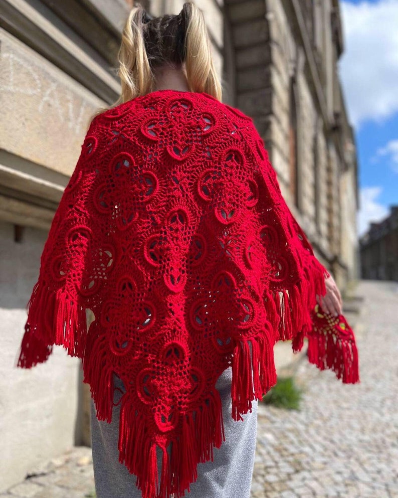 May include: A red crocheted shawl with fringe. The shawl has a delicate pattern and is made with a soft yarn.