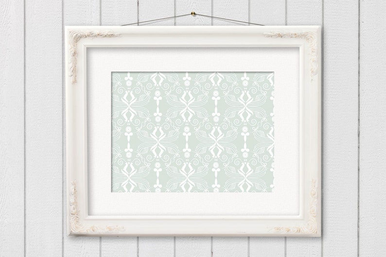 Pu&ograve; includere: Una cornice bianca con un design decorativo e ornato. La cornice &egrave; appesa a una parete di legno bianco e contiene uno sfondo blu chiaro con un motivo floreale bianco.