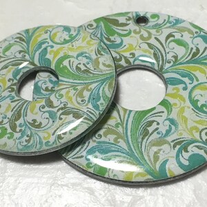 May include: Two round, white, ceramic, decorative pieces with a green, blue, and yellow floral pattern. The pieces have a hole in the center.