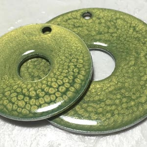 May include: Two green metal washers with a textured surface and a hole in the center. The washers are different sizes.