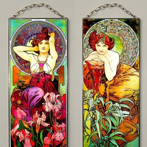 Könnte beinhalten: Vier gerahmte Bleiglasfenster mit Illustrationen von Frauen im Jugendstil mit floralen Motiven. Die Fenster sind in einem silbernen Rahmen mit einer Kette zum Aufhängen. Die Frauen sind in verschiedenen Posen dargestellt, umgeben von Blumen und Blättern. Die Fenster sind ein lebendiges Farbenspiel, darunter Rot, Orange, Gelb, Grün und Blau.
