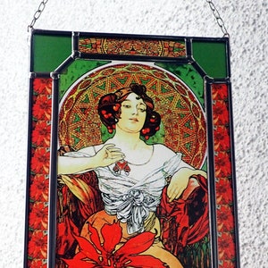 Könnte beinhalten: Ein Buntglasfenster, das eine Frau in einem weißen Kleid mit roten Blumen zeigt. Die Frau sitzt auf einem Stuhl vor einem roten und goldenen Hintergrund mit Mustern. Das Fenster ist in Schwarz und Grün gerahmt.