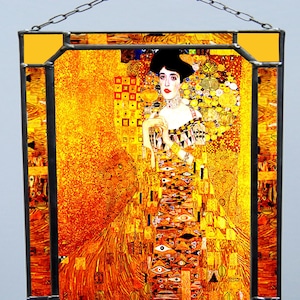 May include: A stained glass window depicting a woman in a gold dress with a geometric pattern. The background is a mosaic of gold, orange, and yellow squares and circles.