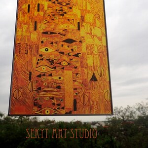 May include: A stained glass window hanging from chains, featuring a colorful abstract design with geometric shapes and eyes. The window is framed in black and has a gold and orange color scheme. The text "SEKYT ART STUDIO" is visible at the bottom of the image.