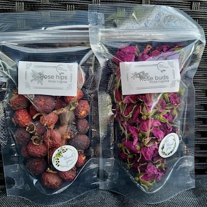 May include: Two clear plastic bags filled with dried rose hips and rose buds. The bags are labeled "100% Natural Rose hips Rosa rugosa" and "100% Natural Rose buds Rosa rugosa".