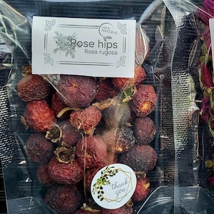 Könnte beinhalten: Transparenter Beutel gefüllt mit getrockneten Hagebutten. Das Etikett trägt die Aufschrift "Rose hips" und "Rosa rugosa". Ein kleiner Aufkleber mit der Aufschrift "thank you" ist ebenfalls sichtbar. Die Hagebutten sind rot.