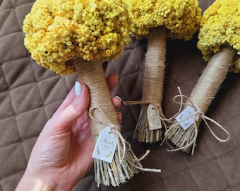May include: Three bouquets of dried yellow flowers with brown twine-wrapped stems. Each bouquet has a tag that says "Thank You". The flowers are on a brown, textured surface.