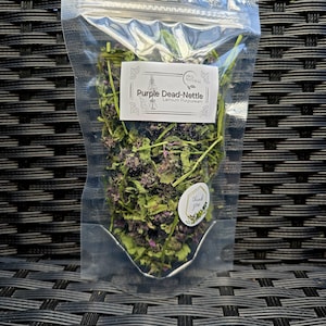 Könnte beinhalten: Ein transparenter Plastikbeutel gefüllt mit getrockneter Purpur- Taubnessel, auch bekannt als Lamium purpureum. Der Beutel hat ein Etikett mit der Aufschrift "100% Natürlich" und "Purpur- Taubnessel Lamium Purpureum". Es gibt auch einen kleinen Aufkleber mit der Aufschrift "Danke".