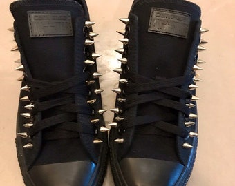 May include: Black Converse All Star sneakers with silver spikes. The shoes have black laces and a black rubber sole.