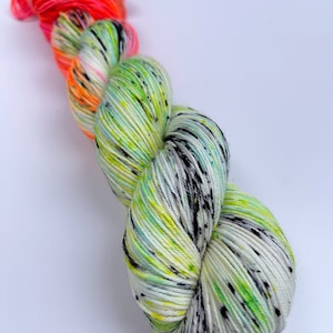 Puede incluir: Un ovillo de hilo con una base blanca y salpicaduras de verde, amarillo y negro. El hilo est&aacute; rematado con una secci&oacute;n de color rosa y naranja brillante.