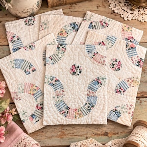 May include: A collection of rectangular fabric quilt blocks featuring a white background with quilted texture. Each block displays curved, pieced sections in various floral and striped patterns in shades of blue, pink, yellow, and green.