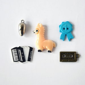 Puede incluir: Surtido de botones coloridos con un llama, un acordeón, una cinta de casete, un amuleto de bellota y una cinta azul con el número "1" en ella.