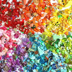 Puede incluir: Un surtido arcoíris de botones, abalorios y baratijas de plástico de colores. Los botones están dispuestos en un patrón de arcoíris, comenzando por el rojo y terminando por el azul. Los botones son de diferentes formas y tamaños, y algunos tienen pequeños detalles como flores, animales y corazones.