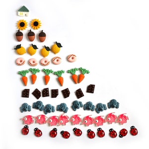 May include: A colorful assortment of small, plastic buttons arranged in a pyramid shape. The buttons feature various designs, including houses, sunflowers, acorns, lemons, donuts, carrots, chocolate bars, jellyfish, fish, and ladybugs.