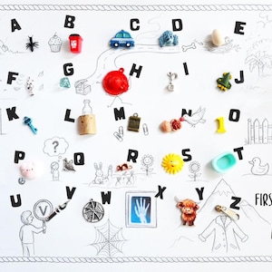 May include: A white educational poster titled First iSpy ABC ANT featuring black line drawings of various scenes and objects arranged alphabetically from A to Z, with small colorful plastic miniature items placed next to each corresponding letter.